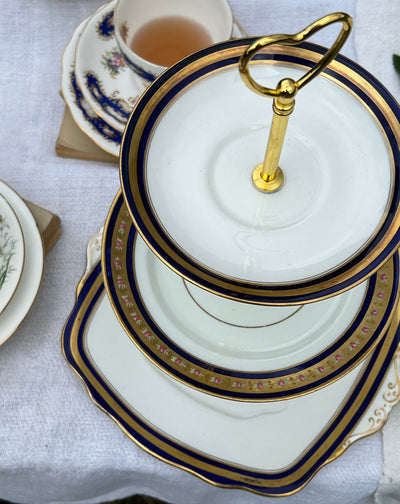 Alzata da dolce a tre piani in porcellana vintage con decoro floreale e bordo dorato e blu.