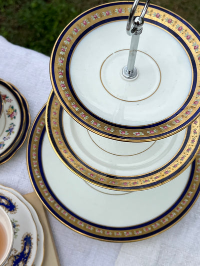 Alzata da dolce a tre piani in porcellana vintage con decoro floreale e bordo blu e dorato.