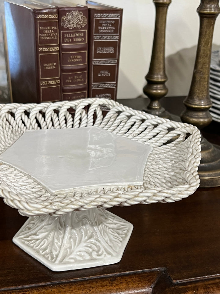 Alzata in ceramica bianca realizzata in Italia con bordo traforato effetto corda intrecciata con base decorata con motivo fogliaceo.

Perfetta da utilizzare come portafrutta o per servire dolcetti.

Misure 24x11 cm