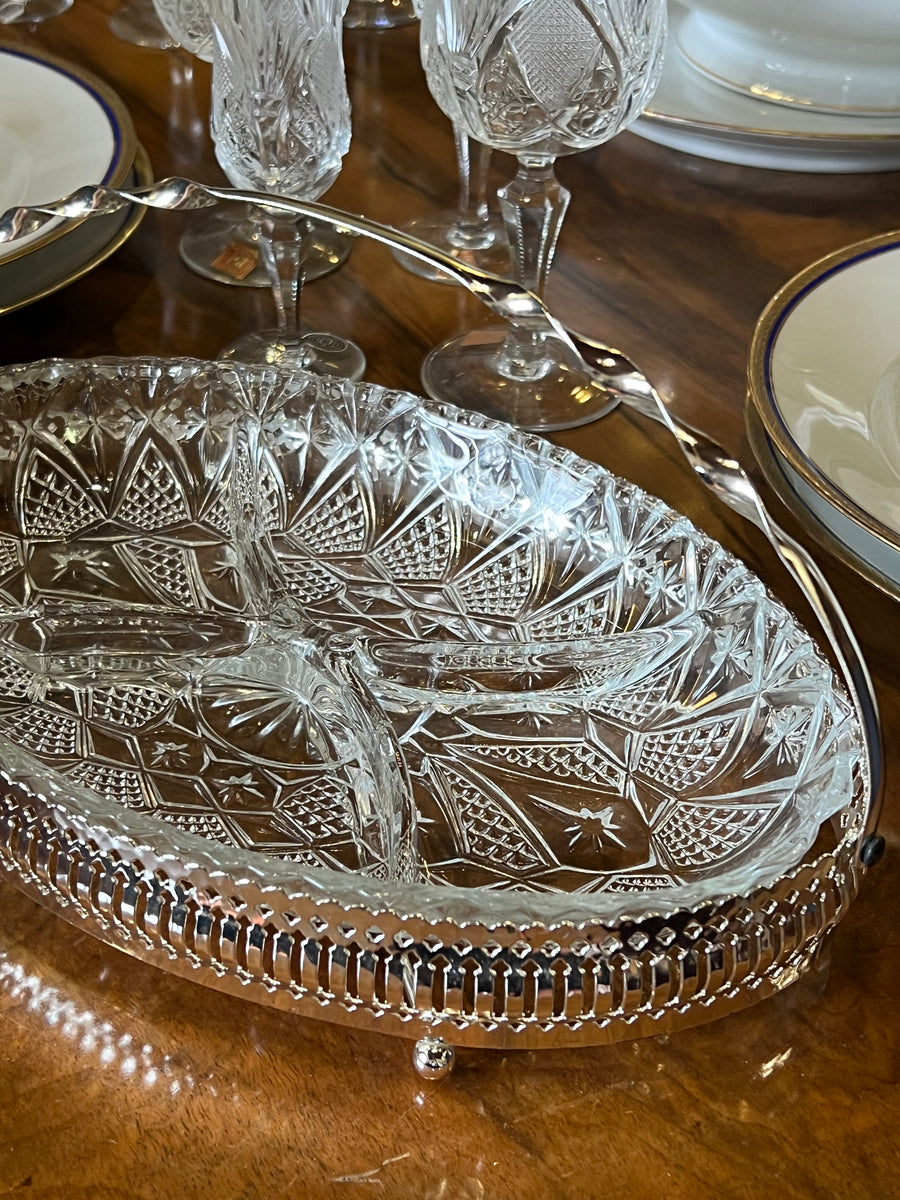 Deliziosa antipastiera realizzata in vetro lavorato completo di vassoio in metallo &nbsp;con manico. Il bordo della base in silverplate presenta un motivo traforato con una finitura lucida, che conferisce un tocco di classe e luminosità.

Questo pezzo è perfetto per servire antipasti, stuzzichini o piccoli dolci durante una cena o un'occasione speciale.

Misure 31x20x5 cm