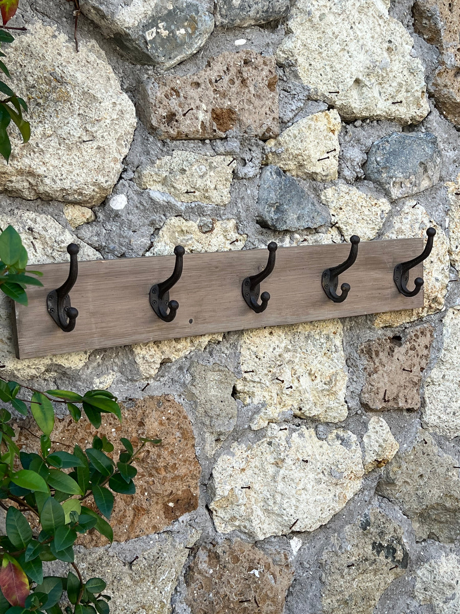 Appendiabiti da parete in legno chiaro con 5 ganci doppi in ferro brunito montato su muro in pietra