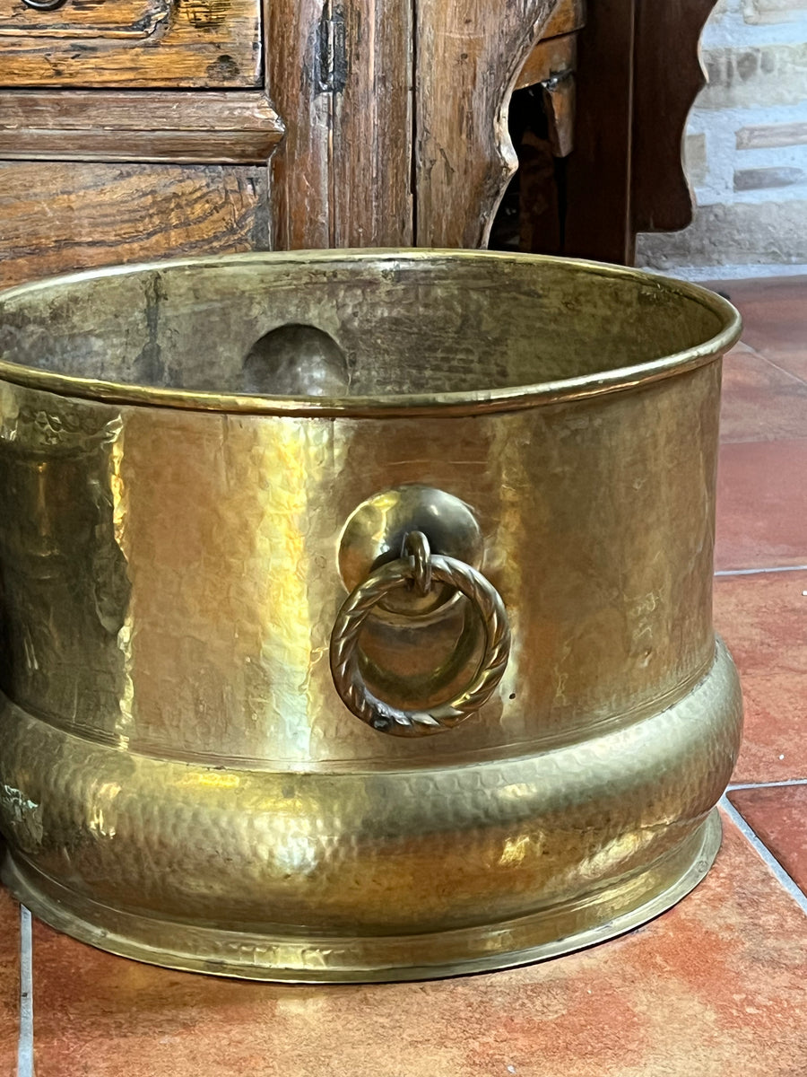 Cachepot vintage in ottone martellato con manici ad anello intrecciato, ambientato su pavimento rustico