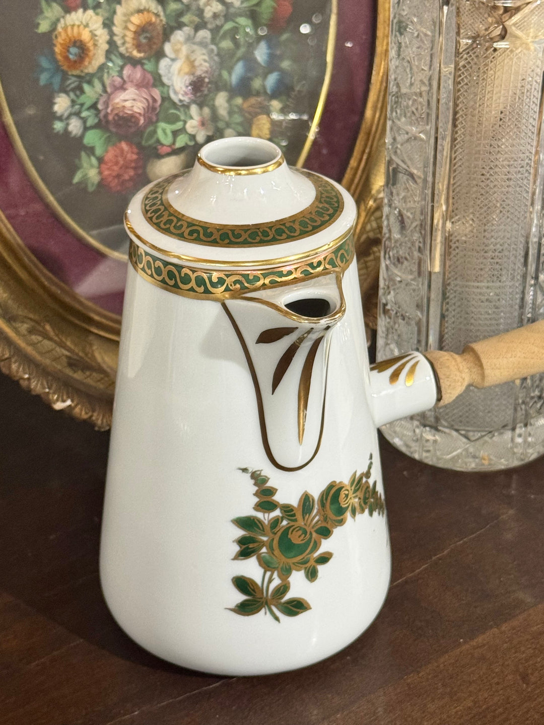Cioccolatiera vintage in porcellana bianca con decori floreali verde e oro e manico laterale in legno.