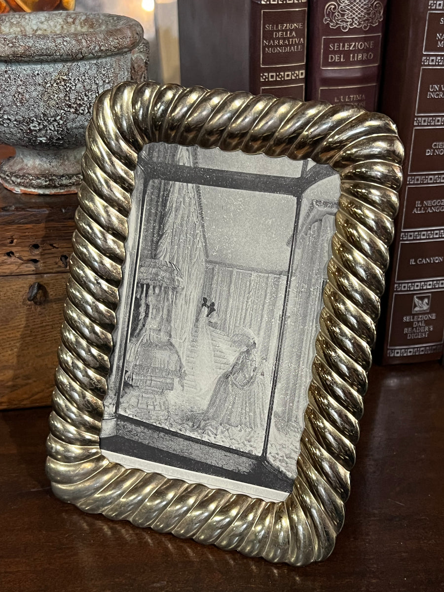 Elegante Cornice portafoto in silverplate dorato caratterizzato da un design ricco e raffinato, con un bordo a rilievo intrecciato che dona al pezzo un tocco di lusso e classicità.

Le curve morbide e la finitura dorata lucida fanno sì che la cornice si distingua come un elemento decorativo di grande effetto, ideale per esporre fotografie o immagini d’epoca.

Misure 18x13x1 cm