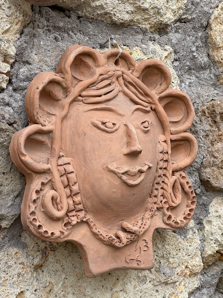 Decorazione da parete in terracotta raffigurante volto femminile appeso su muro in pietra