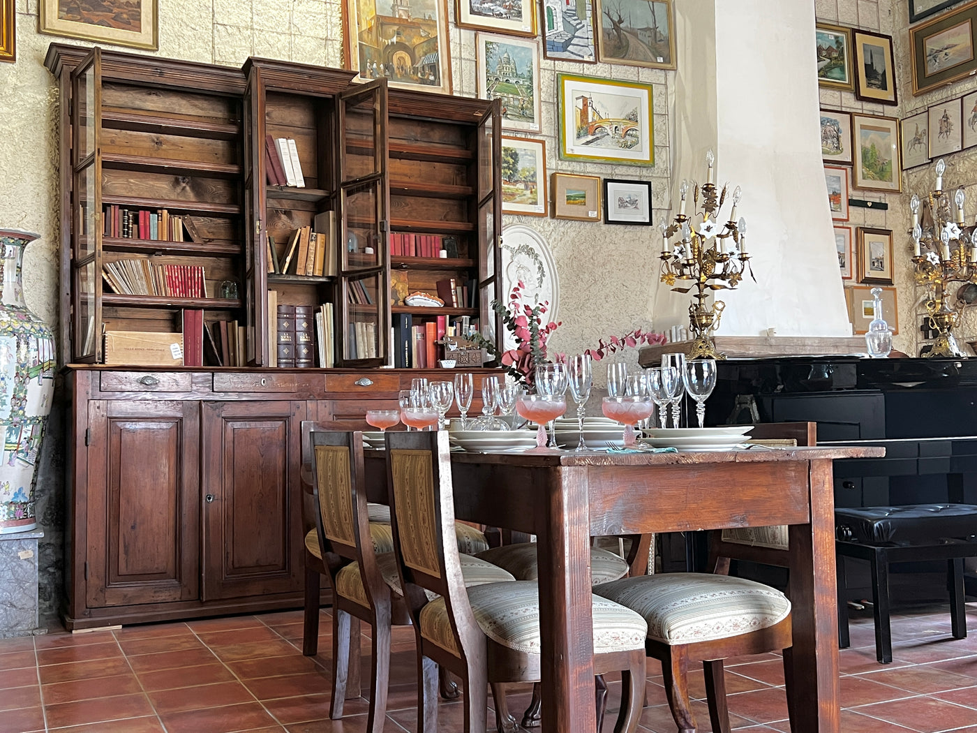 Ingresso del negozio vintage: un pianoforte giapponese kawai , una grande biblioteca francese in rovere ed un tavolo apparecchiato elegantemente con un servizio di bicchieri in cristallo vintage e dei piatti ginori. sulle pareti quadri e stampe d'epoca