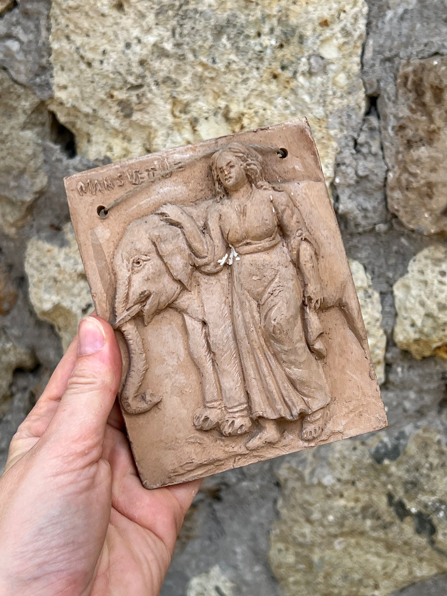Mattonella da parete in terracotta raffigurante una scena in rilievo con un elefante e una figura femminile.

La lavorazione artigianale e i dettagli espressivi rendono questo pezzo un affascinante elemento decorativo.

Misure 10x13 cm&nbsp;