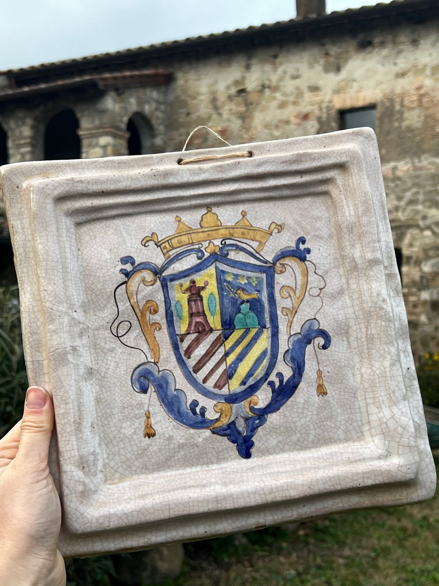 Mattonella decorativa da parete in ceramica smaltata con decoro dipinto a mano raffigurante uno stemma. L'oggetto presenta una finitura craquelé che ne accentua il fascino vintage e il carattere artigianale. Aggiunge un tocco di storia e autenticità a qualsiasi ambiente, sia classico che moderno.

Misure 27x29 cm