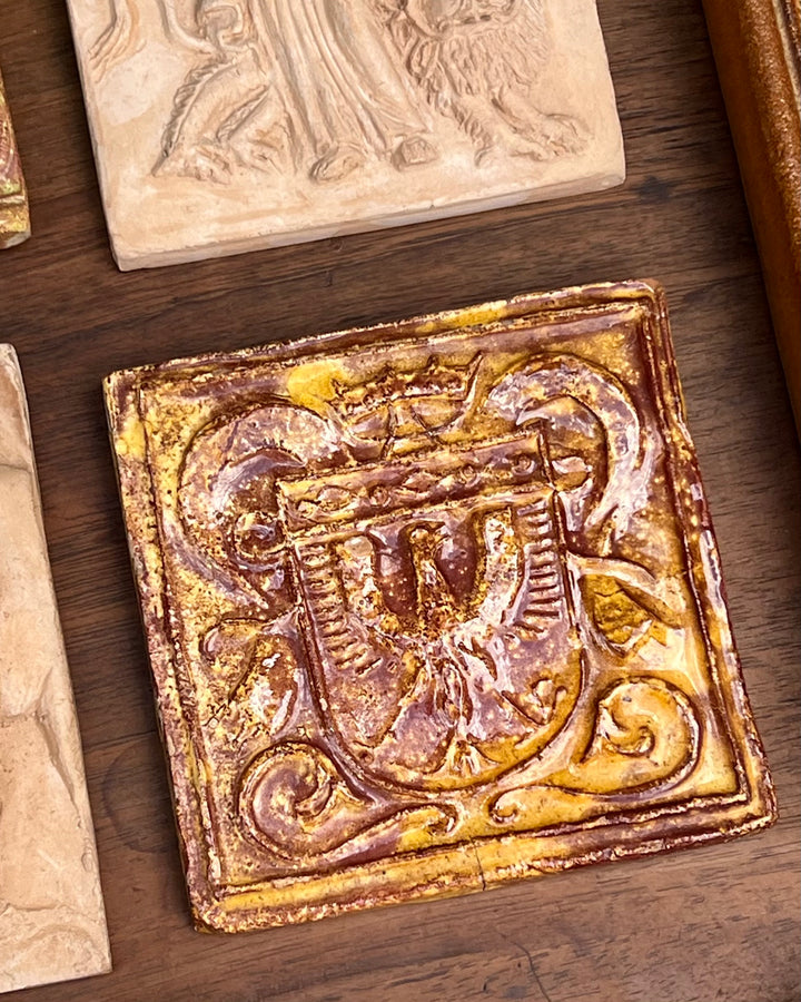 Mattonella decorativa in terracotta smaltata con motivo fregio sulla parte frontale sui toni del marrone e arancione.

La superficie presenta una patina del tempo che ne accresce il fascino vintage.&nbsp;

Misure 11,5x11,5 cm