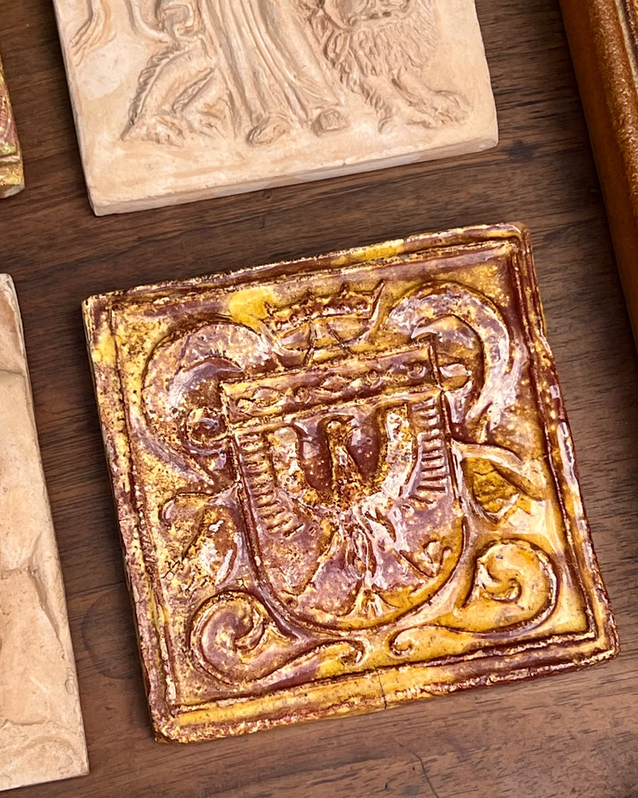 Mattonella decorativa in terracotta smaltata con motivo fregio sulla parte frontale sui toni del marrone e arancione.

La superficie presenta una patina del tempo che ne accresce il fascino vintage.&nbsp;

Misure 11,5x11,5 cm