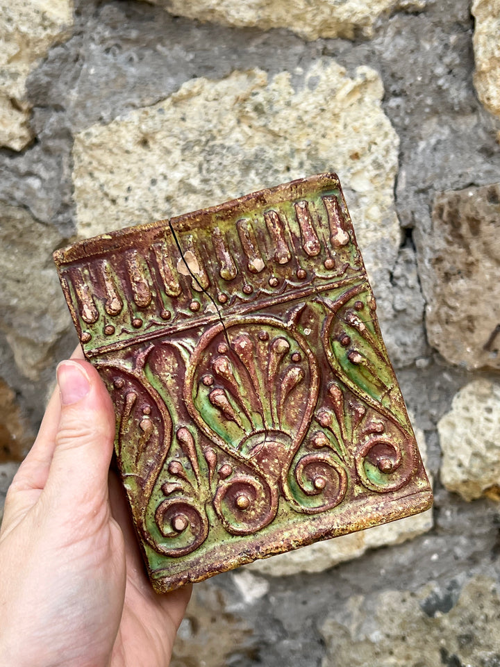 Mattonella decorativa in terracotta smaltata con motivi floreali e geometrici in rilievo, realizzata nei toni del verde e del marrone.

La superficie presenta una patina del tempo che ne accresce il fascino vintage.&nbsp;

Misure 10,5x12,5 cm