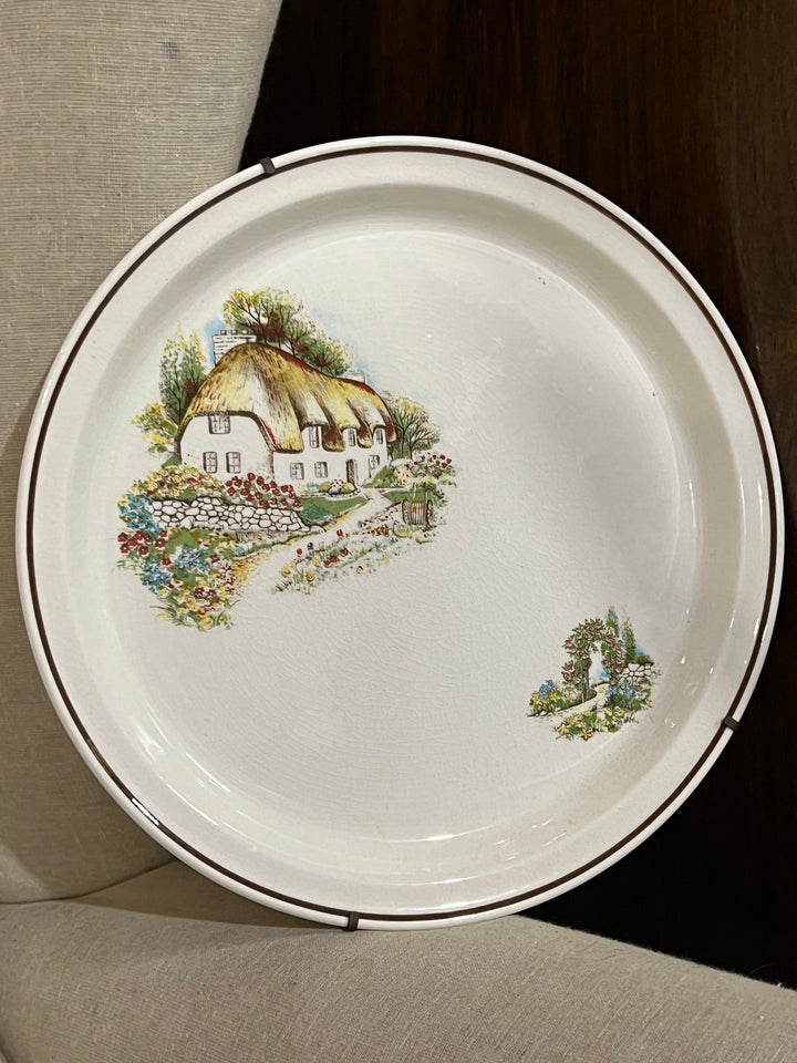 Piatto da parete in ceramica decorata con una scena idilliaca raffigurante un cottage inglese immerso in un giardino fiorito. La raffinata decorazione richiama la quiete e il fascino della campagna inglese.

Diametro 27 cm&nbsp;