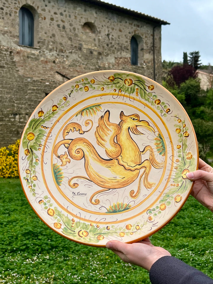 Piatto da parete in ceramica decorato a mano, proveniente da Cerreto Sannita. Il motivo centrale raffigura un elegante animale fantastico dalle tonalità gialle, circondato da ornamenti floreali stilizzati sui toni del verde e del giallo. La firma "Di Lorenzo" sulla parte frontale ne attesta l'origine artistica ed artigianale.

Misure Diametro 42 cm&nbsp;