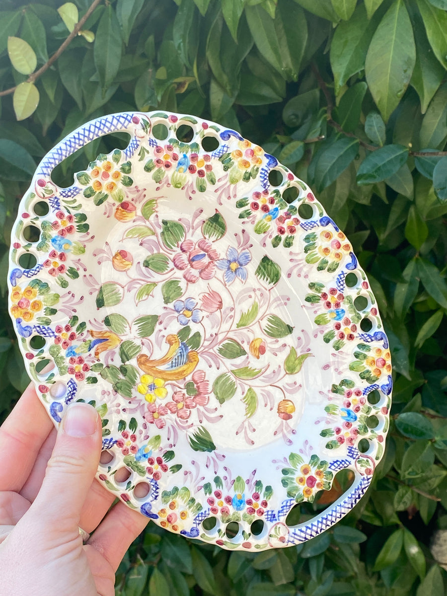 Piatto di forma ovale in ceramica portoghese, arricchito da una bella decorazione floreale policroma dipinto a mano ed intagli nella parte esterna.  Misure 21x16 cm