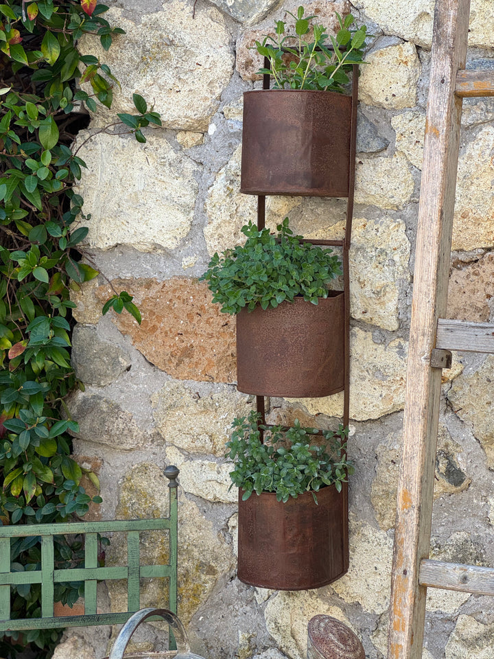 Porta vasi verticale in ferro con tre contenitori appeso a muro in pietra con piante aromatiche
