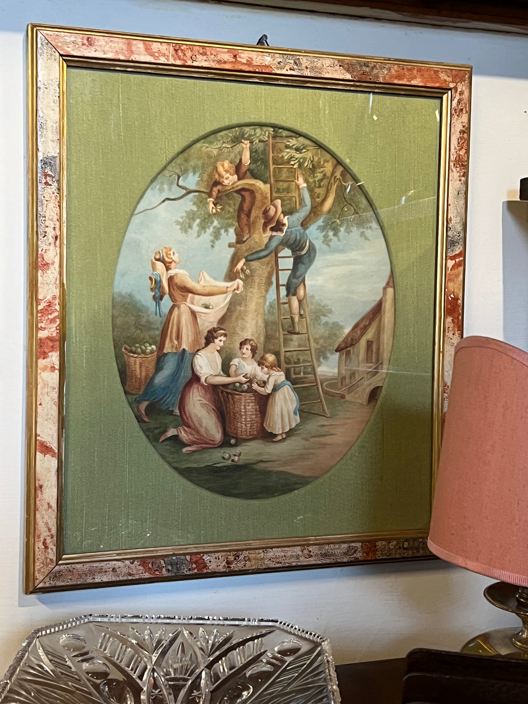 Quadro realizzato con tecnica mista acquarello e matita raffigurante una scena di vita campestre catturando la freschezza e vivacità di una giornata in campagna. La scena è arricchita con dettagli meticolosi e colori vividi che raffigurano figure in movimento tra gli alberi nella raccolta di frutti. Le figure, abbigliate in abiti tradizionali del periodo, sono immerse in un paesaggio rurale idilliaco, con un cottage sullo sfondo.

