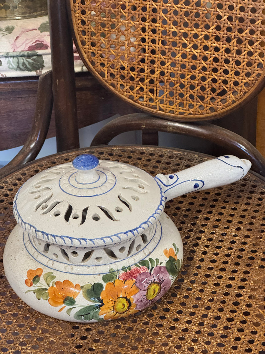 Scaldino vintage in ceramica di Bassano con lungo manico, coperchio traforato e decorazioni floreali gialle e viola su fondo avorio.