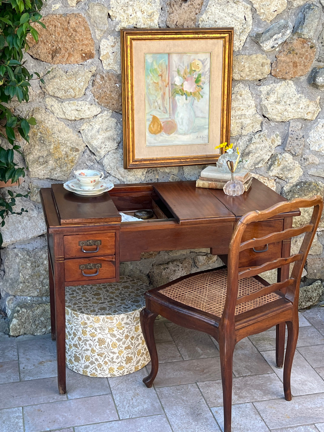 Scrittoio vintage in noce con tre cassetti, piano a ribalta e sedia in paglia di Vienna, ambientato davanti a muro in pietra