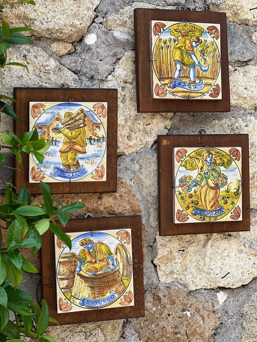 Set di quattro mattonelle in ceramica dipinta raffiguranti le stagioni, firmate Sutri, montate su cornici in legno