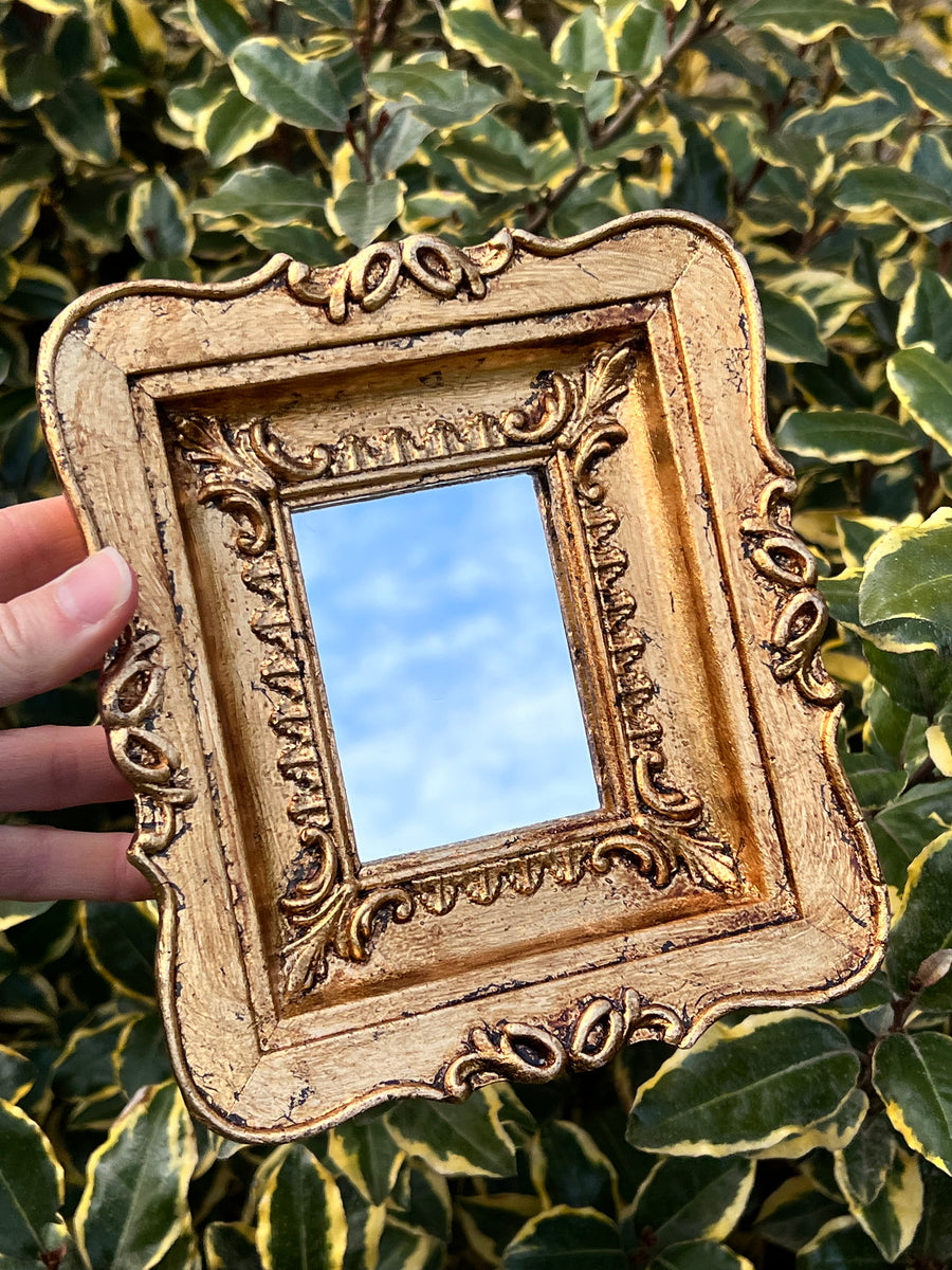 Specchietto di misure 18,5x16 cm, di ispirazione barocca con cornice intagliata e dorata a foglia oro. Lungo tutta la cornice è presente un rifinito decoro a rilievo. Con una maestria che trascende il tempo, i nostri specchietti sono capolavori realizzati a mano che catturano l'essenza dell'eleganza barocca. Ogni cornice, finemente scolpita e rifinita con foglia d'oro, è frutto di tecniche di antichizzazione che regalano un'anima vissuta e senza tempo ad ogni pezzo.