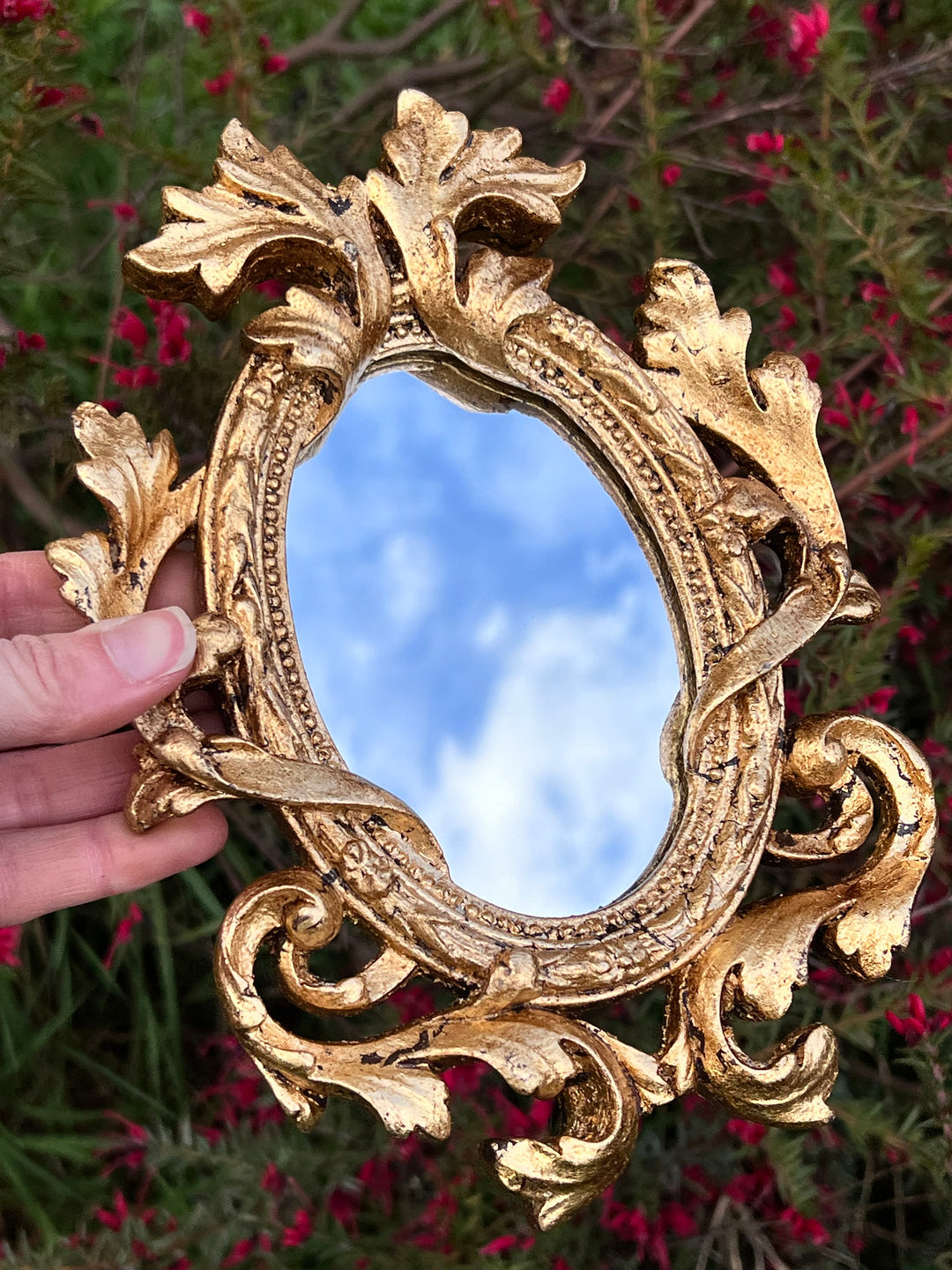 Specchietto di misure 16x21 cm, di ispirazione barocca con cornice intagliata e dorata a foglia oro. Lungo tutta la cornice è presente un elaborato decoro fogliaceo. Con una maestria che trascende il tempo, i nostri specchietti sono capolavori realizzati a mano che catturano l'essenza dell'eleganza barocca. Ogni cornice, finemente scolpita e rifinita con foglia d'oro, è frutto di tecniche di antichizzazione che regalano un'anima vissuta e senza tempo ad ogni pezzo.