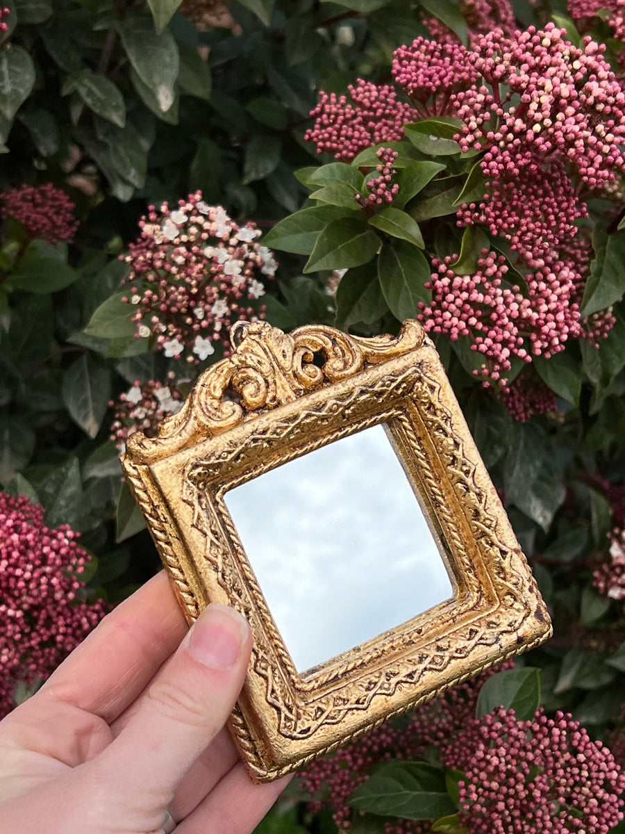 Specchietto di misure 12x10 cm, con cornice intagliata e dorata a foglia oro. Nella parte superiore è presente un dettaglio a fregio e lungo la cornice un decoro geometrico. Con una maestria che trascende il tempo, i nostri specchietti sono capolavori realizzati a mano che catturano l'essenza dell'eleganza barocca. Ogni cornice, finemente scolpita e rifinita con foglia d'oro, è frutto di tecniche di antichizzazione che regalano un'anima vissuta e senza tempo ad ogni pezzo.