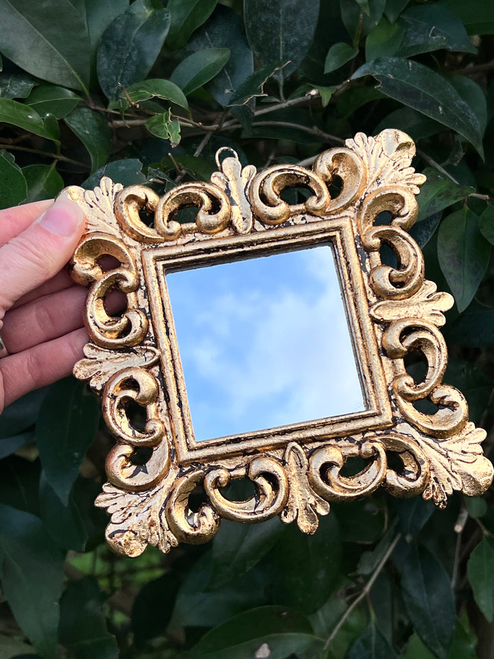 Specchietto di misure 14,5x14,5 cm, di ispirazione barocca con cornice intagliata e dorata a foglia oro. Lungo tutta la cornice è presente un intricato decoro intagliato. Con una maestria che trascende il tempo, i nostri specchietti sono capolavori realizzati a mano che catturano l'essenza dell'eleganza barocca. Ogni cornice, finemente scolpita e rifinita con foglia d'oro, è frutto di tecniche di antichizzazione che regalano un'anima vissuta e senza tempo ad ogni pezzo.