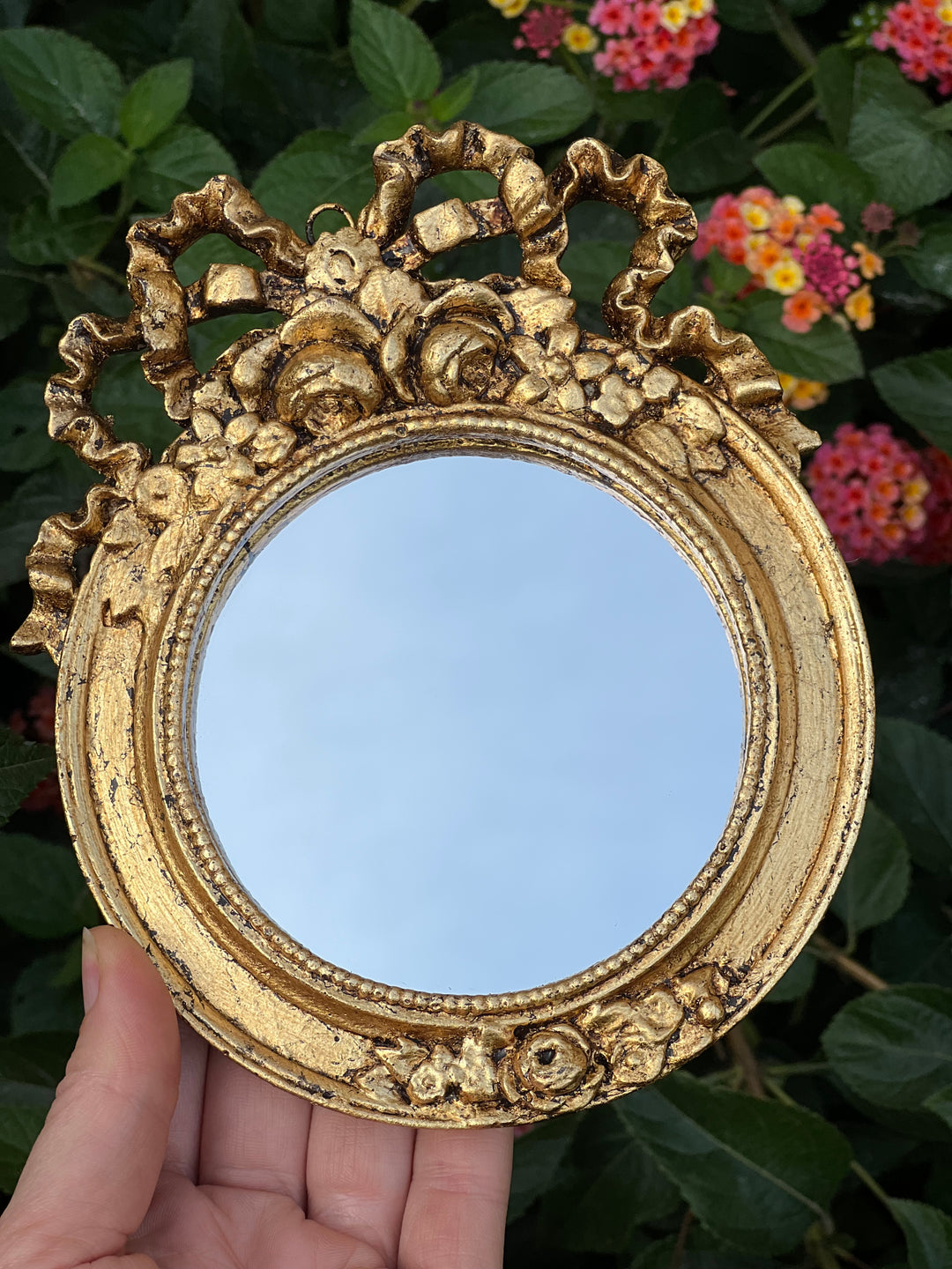 Specchietto di misure 13x16 cm, di ispirazione barocca con cornice intagliata e dorata a foglia oro. Nella parte superiore è presente un dettaglio a fiocchetto mentre nella parte inferiore un intaglio floreale.

Con una maestria che trascende il tempo, i nostri specchietti sono capolavori realizzati a mano che catturano l'essenza dell'eleganza barocca. Ogni cornice, finemente scolpita e rifinita con foglia d'oro, è frutto di tecniche di antichizzazione che regalano un'anima vissuta e senza tempo ad ogni pez