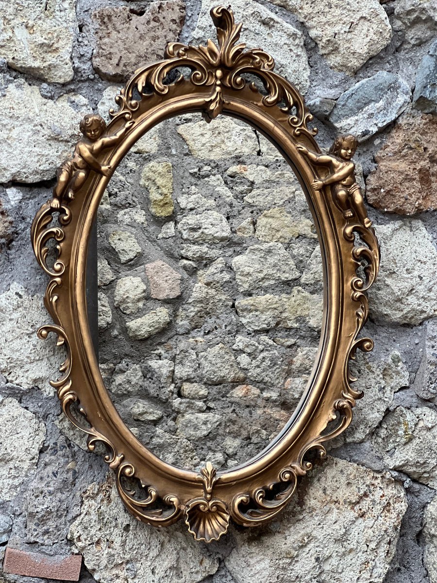 Specchio con cornice ovale dorata lavorata con putti sulla parte superiore e ghirigori lungo tutto il bordo in stile rococò.&nbsp;  In qualche punto la doratura è saltata.  Misure 58x87 cm