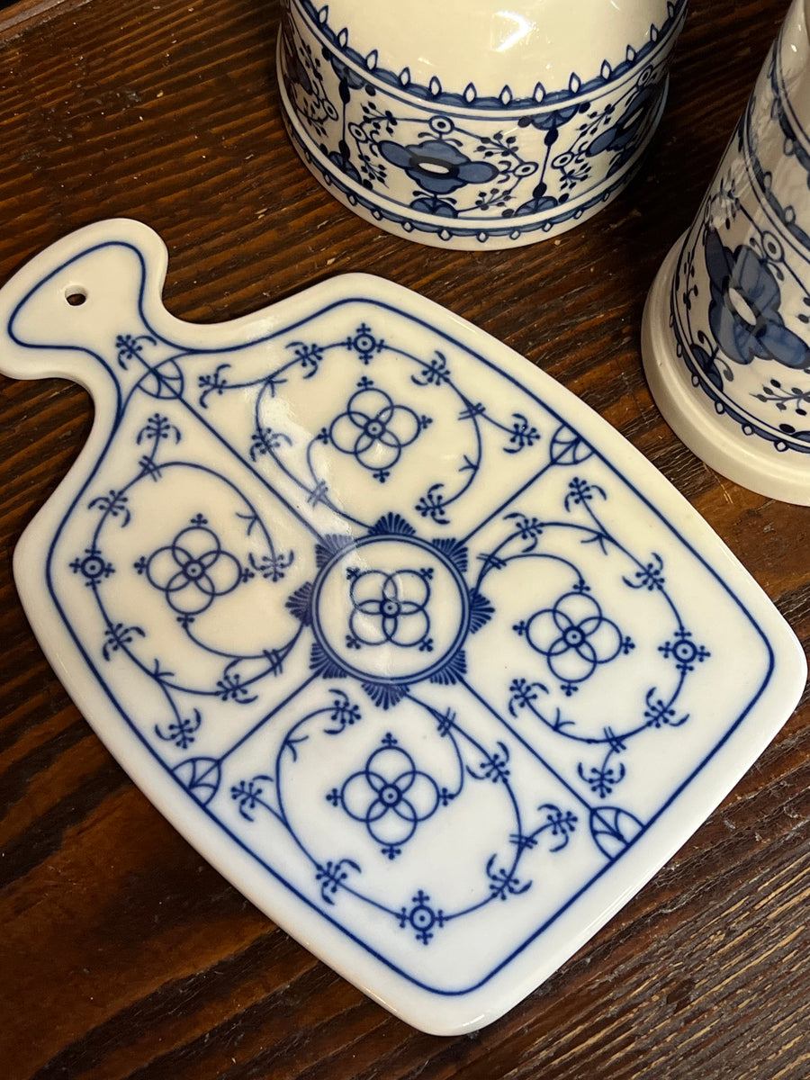 Tagliere in porcellana con decoro blu su fondo bianco in stile tradizionale. Questo pezzo, oltre alla sua funzione pratica, si distingue per il suo design raffinato che lo rende perfetto anche come elemento decorativo in cucina. Il foro superiore permette di appenderlo facilmente, rendendolo anche un'ottima aggiunta estetica per una parete.

Misure 25x16,5 cm
