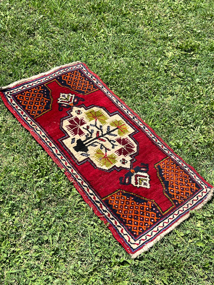 Tappeto persiano Oushak con misure 105x52 cm. &nbsp;  Al centro è raffigurato un bouquet di fiori in stile geometrico su fondo rosso.