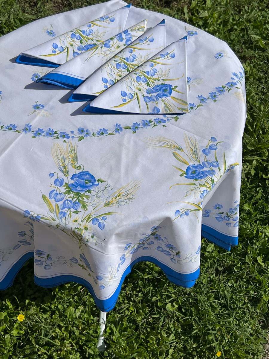 Tovaglia ovale bianca con decoro floreale blu e tovaglioli coordinati apparecchiata in giardino
