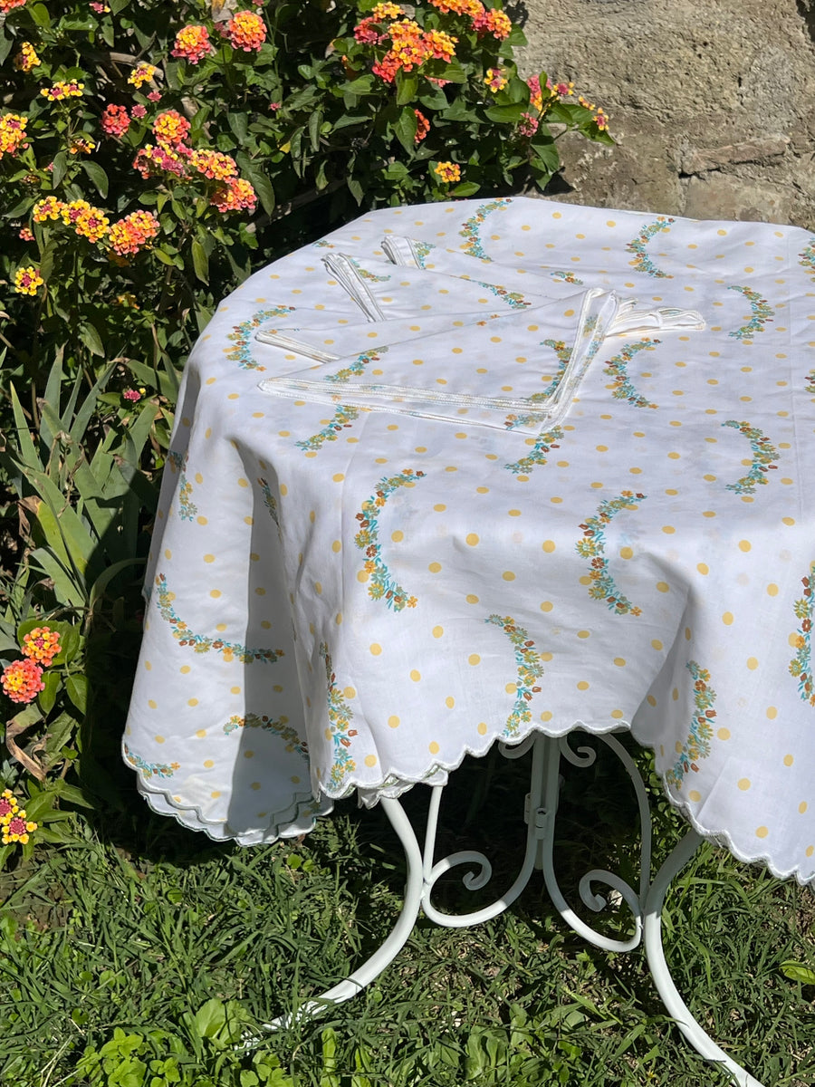 Tovaglia bianca con pois gialli e decorazioni floreali apparecchiata in giardino con tovaglioli coordinati