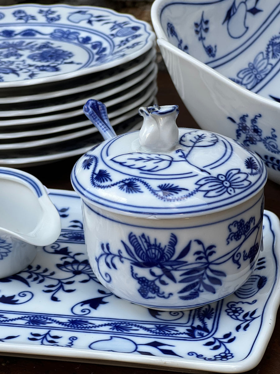 Zuccheriera in porcellana decorata con il celebre motivo "Zwiebelmuster" o "Blue Onion", un classico della tradizione europea. Caratterizzata da eleganti disegni in blu cobalto e completa di coperchio e cucchiaino, questa zuccheriera aggiunge un tocco di raffinatezza alla tavola, sia per l'uso quotidiano che per occasioni speciali. tile.

Misure 10x10 cm cucchiaino 12 cm&nbsp;
