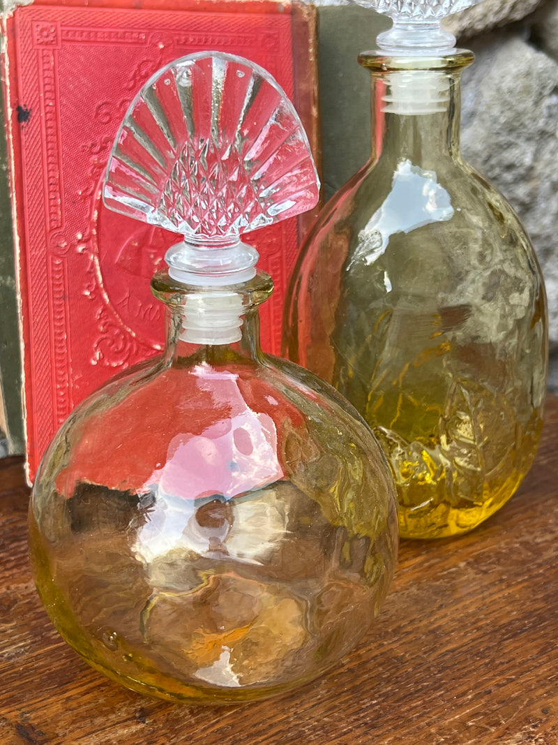 Bottiglia in vetro di colore giallo con tappo in vetro trasparente, di forma tonda.  Presenta una decorazione floreale sulla parte inferiore della bottiglia.